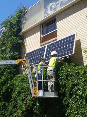 contracting crew lifting up solar panels to the roof while standing on a crane