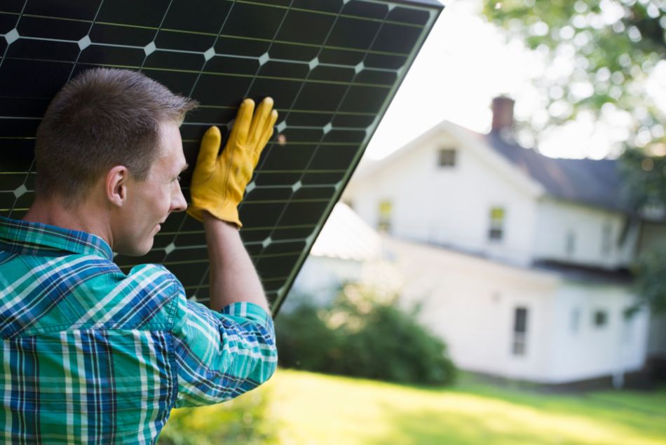 man wearing yellow gloves lifting solar panel on shoulder for home installation