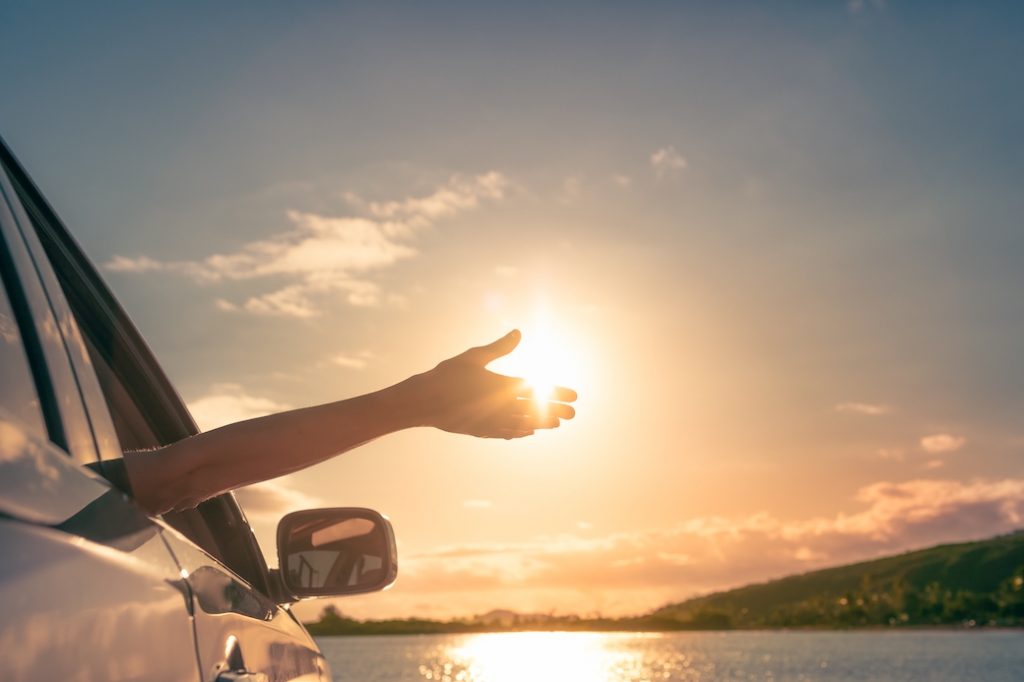person with arm out of window blocking the sun overlooking a lake