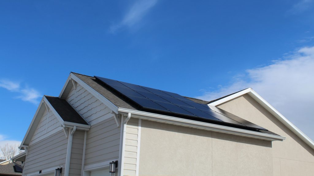 Black solar panels on roof of home with sunny blue sky in background