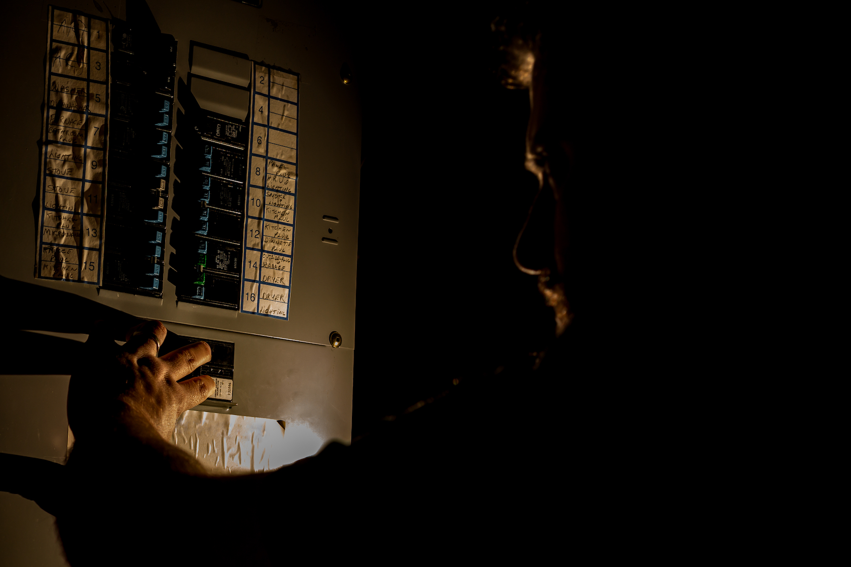 Man visible only by flashlight, looking at home's electric panel during power outage