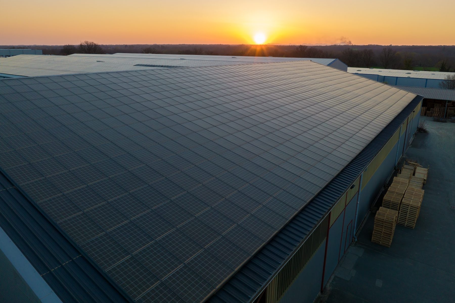 Black photovoltaic solar panels mounted on business's building roof with sunset in background